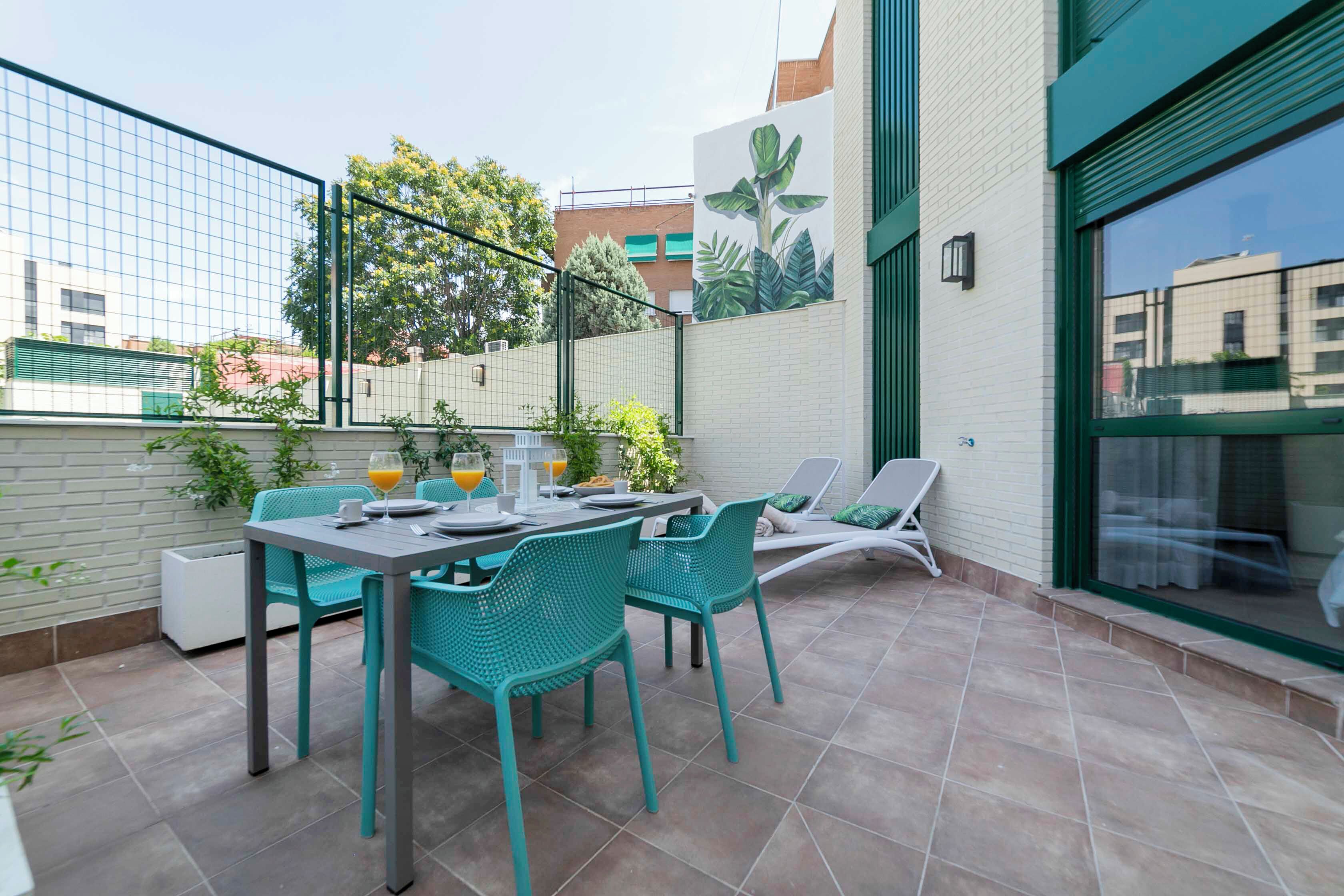 Un patio al aire libre con una mesa y sillas, una cerca blanca y un mural en la pared.