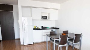 A compact kitchen with white cabinetry, a microwave, and a dining area with a table and chairs. - Rosario Center (Rosario)