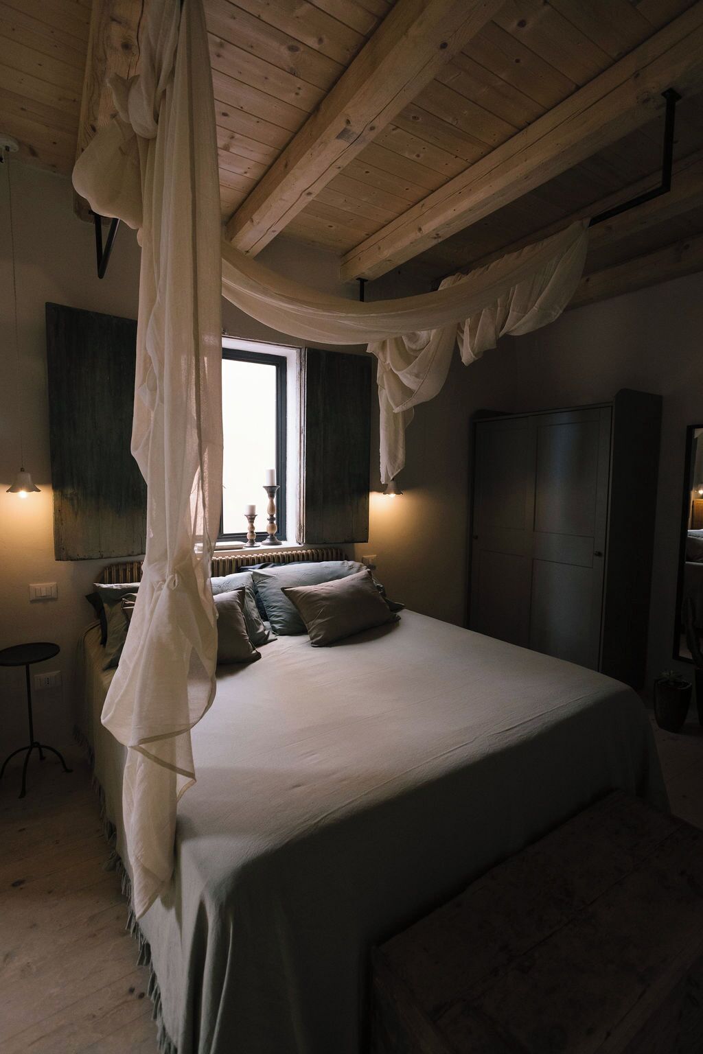 Une chambre à coucher avec un lit à baldaquin, une fenêtre avec des volets, un radiateur et une armoire.