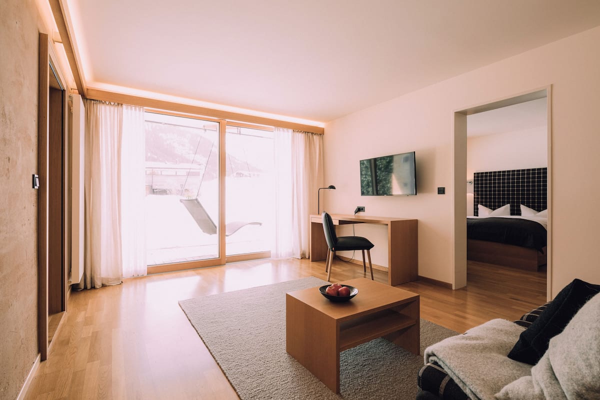 A modern hotel room with a wooden desk, a comfortable sofa, a flat-screen TV, and a bed with a black headboard.