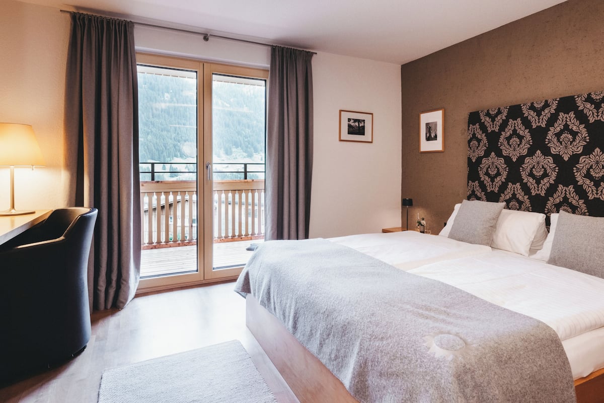 A hotel room with a large bed, a desk, and a view of a balcony.