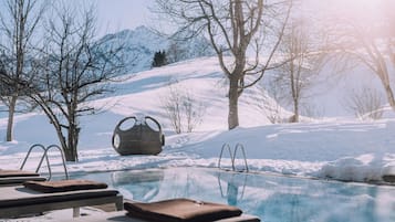 Un área de piscina con sillones de descanso y una original silla esférica, rodeada por un paisaje nevado y árboles.