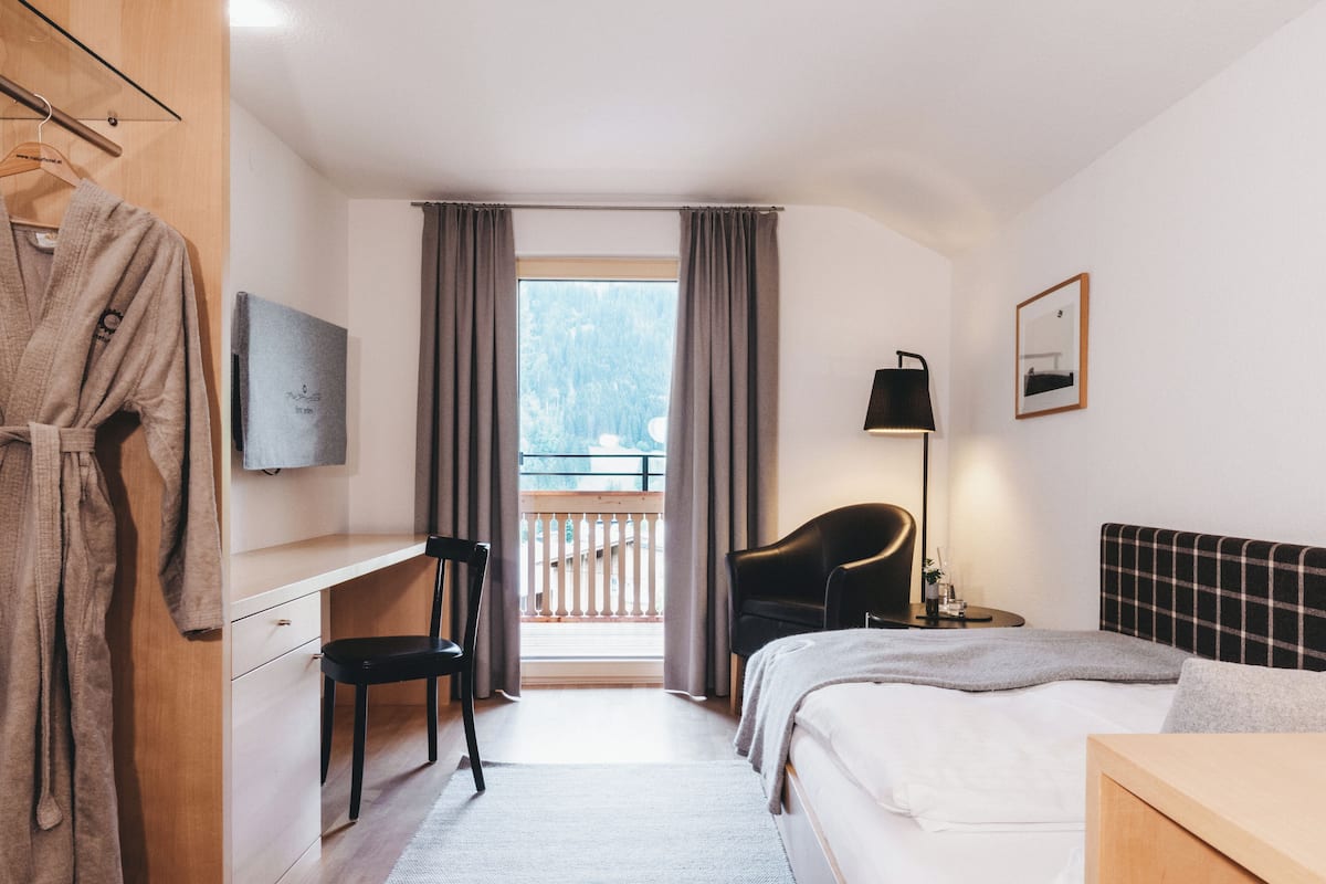 A hotel room with a bed, a desk, a chair, a TV, a lamp, and a balcony with curtains.