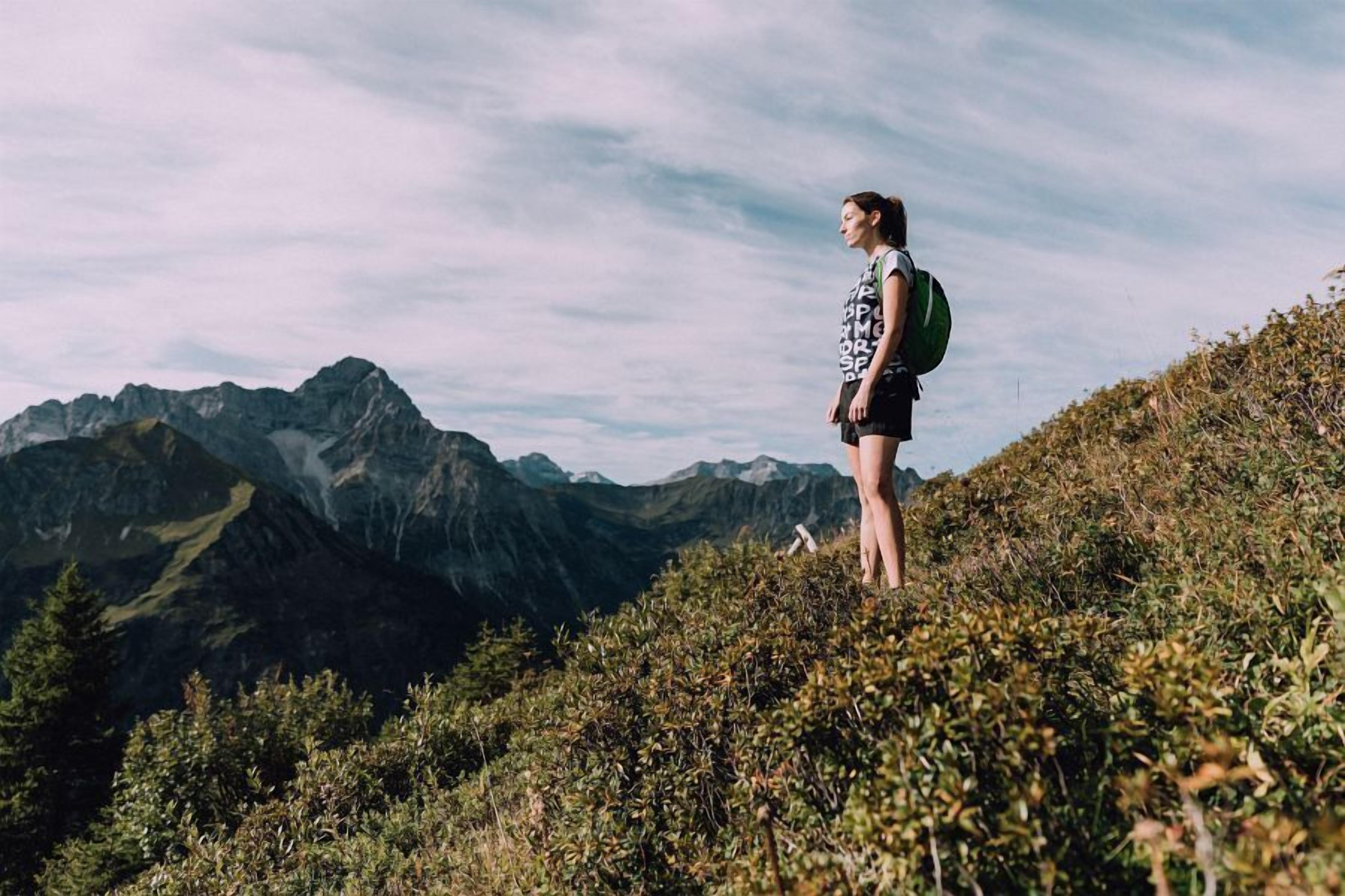 A person standing on a grassy hill with a mountainous landscape in the background.
