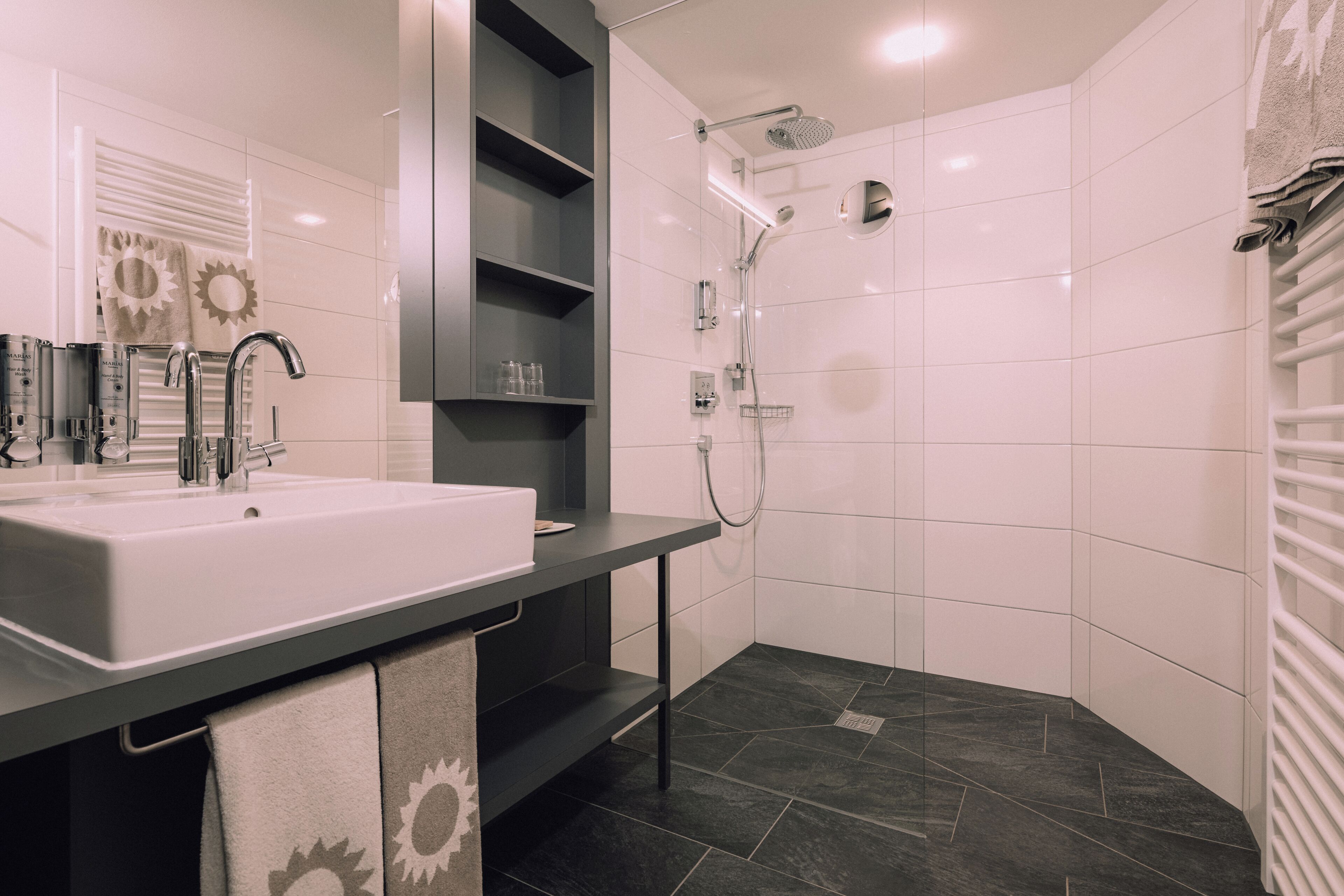 A modern bathroom with a white sink, dark countertop, and a shower area with a glass door.