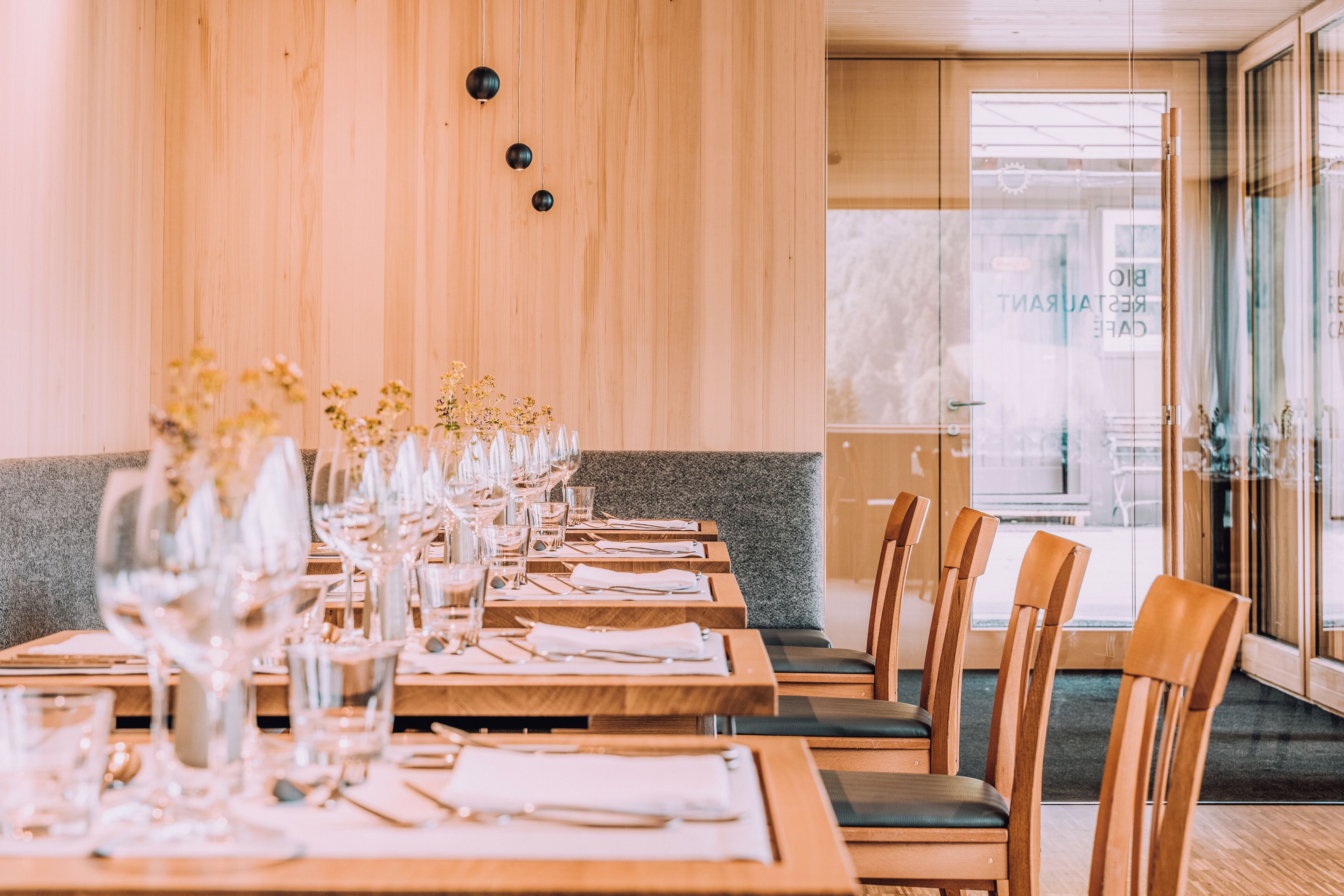 Un restaurante con mesas y sillas de madera, puertas de cristal y una pared de piedra.