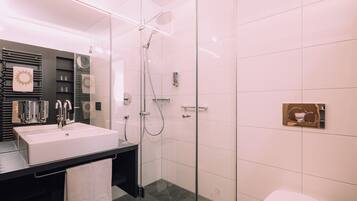 Un baño moderno con cabina de ducha de vidrio, un lavamanos blanco y un inodoro.