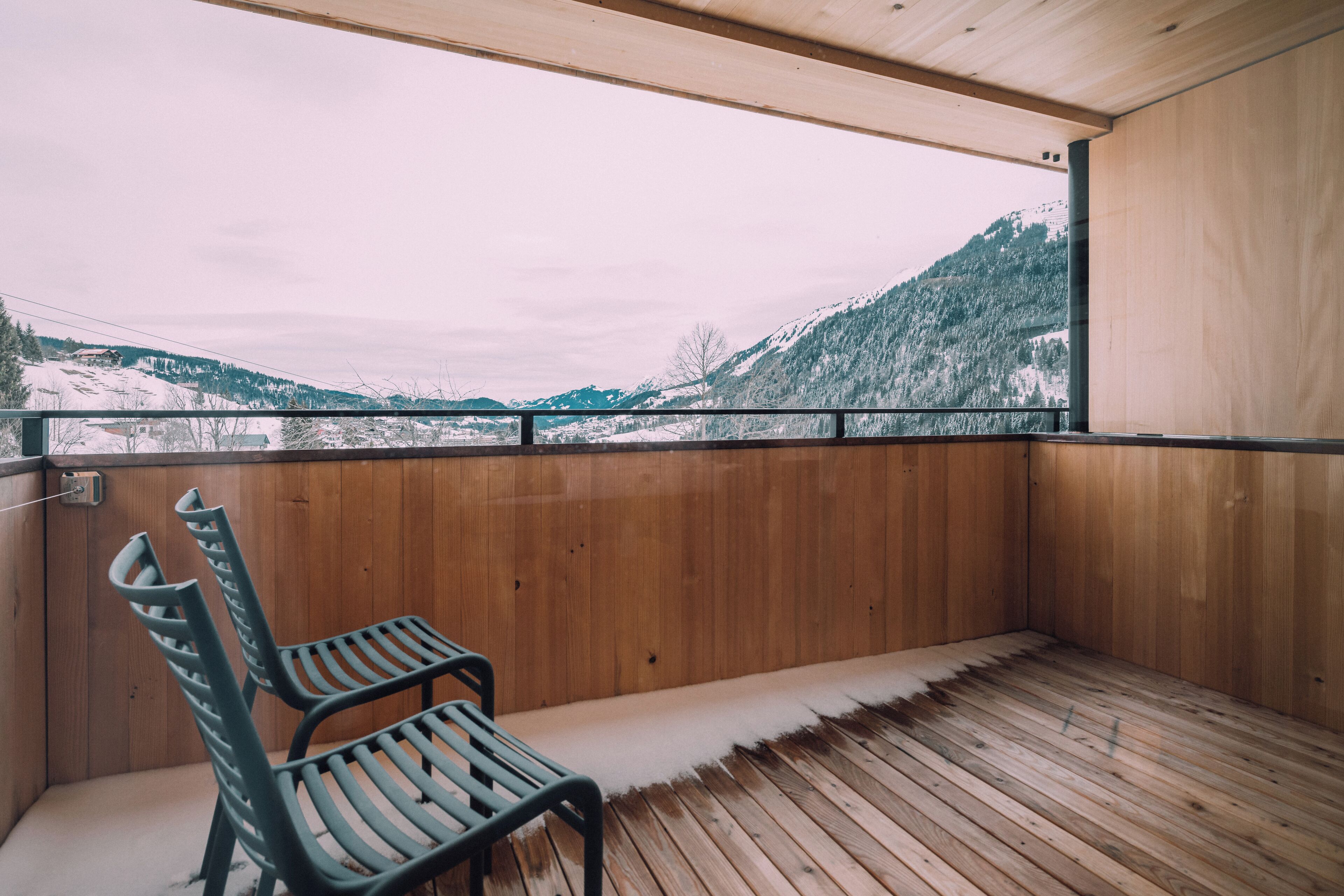 A wooden deck with a bench, a view of snow-covered mountains, and a wooden wall.