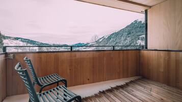 A wooden deck with a bench, a view of snow-covered mountains, and a wooden wall.