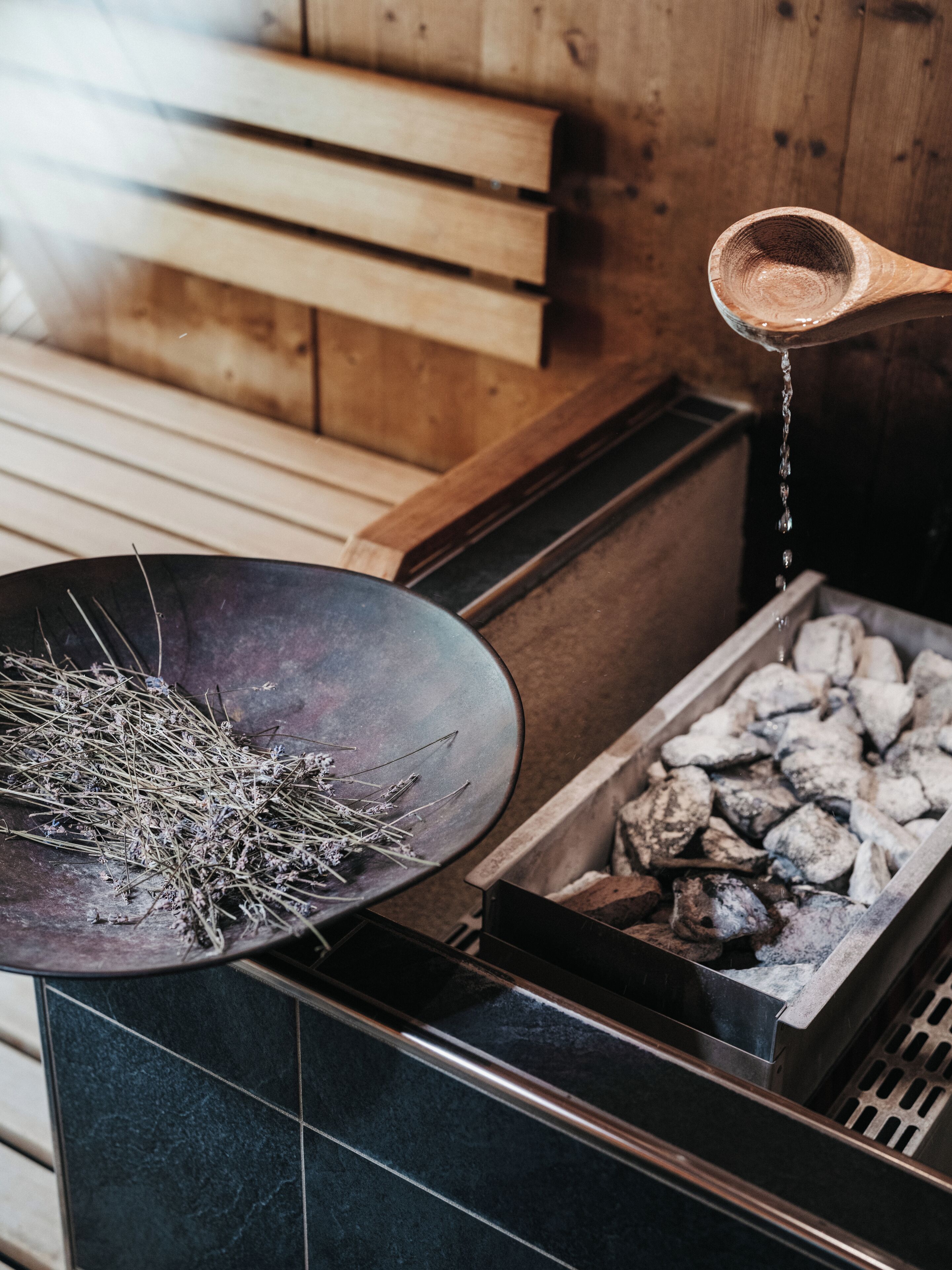 Un sauna avec un banc en bois, un récipient noir rempli d’herbes et un pot de charbon de bois.