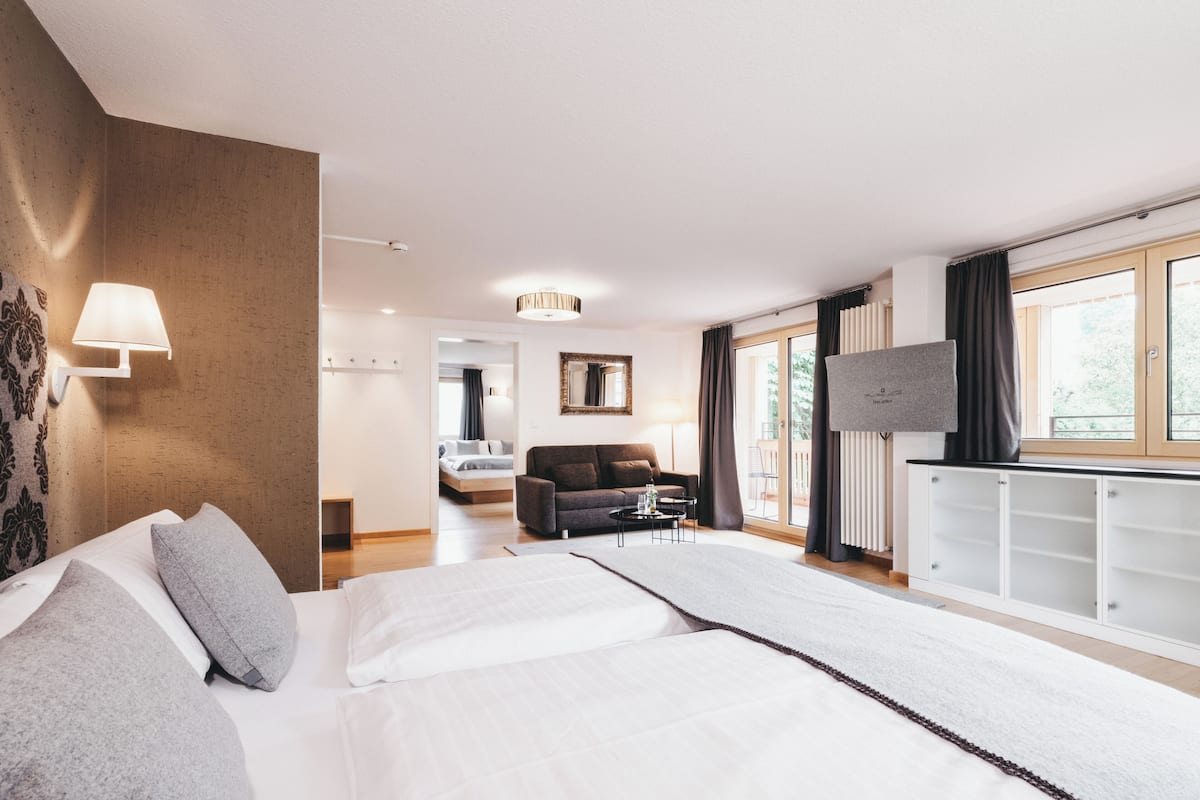 A modern hotel room with a large bed, a sofa, a TV, and a view of the outdoors.