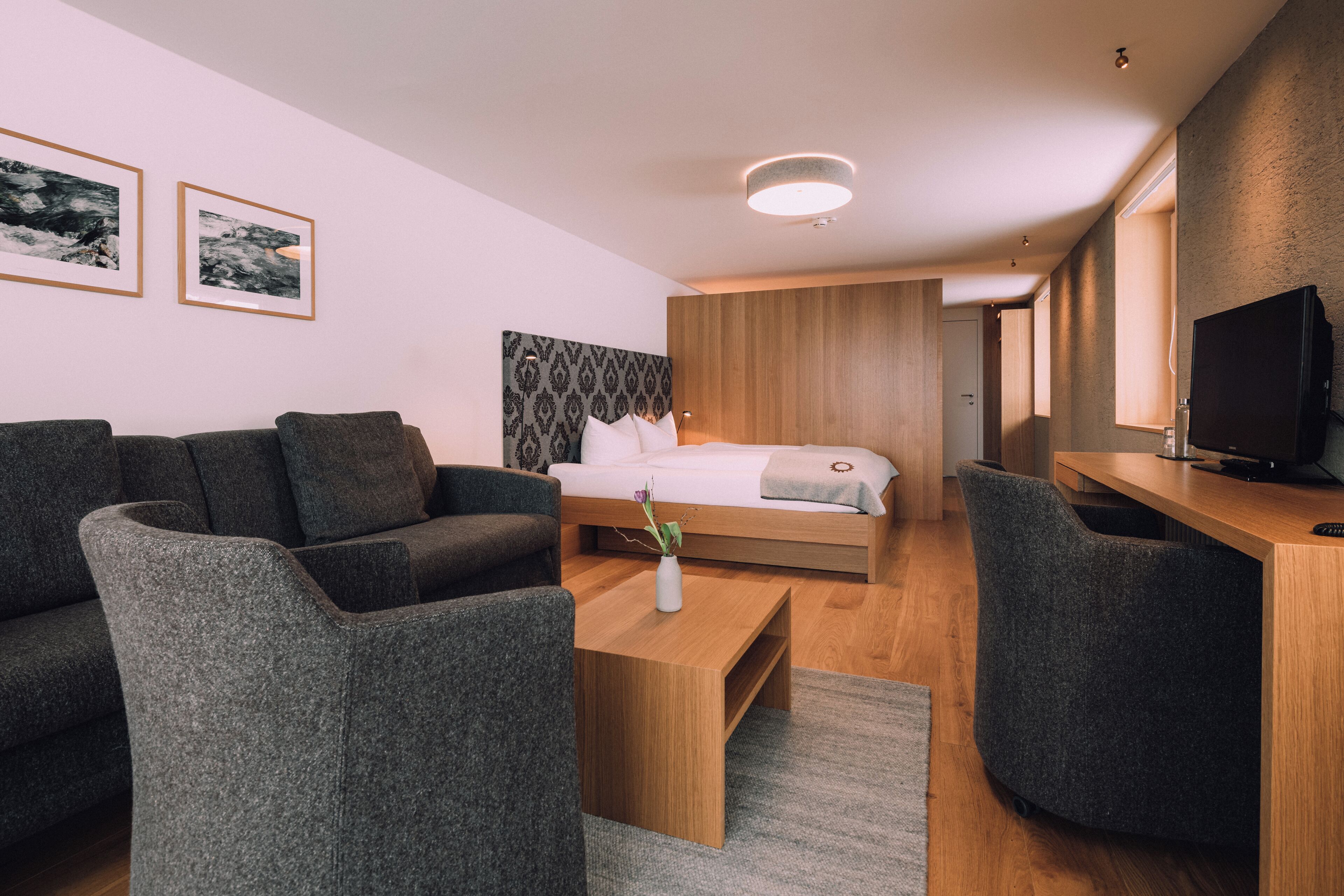 Una habitación de hotel moderna con cama, sofá, mesa de centro y televisión.