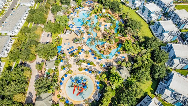 An aerial view of a resort with multiple swimming pools, palm trees, and modern buildings.