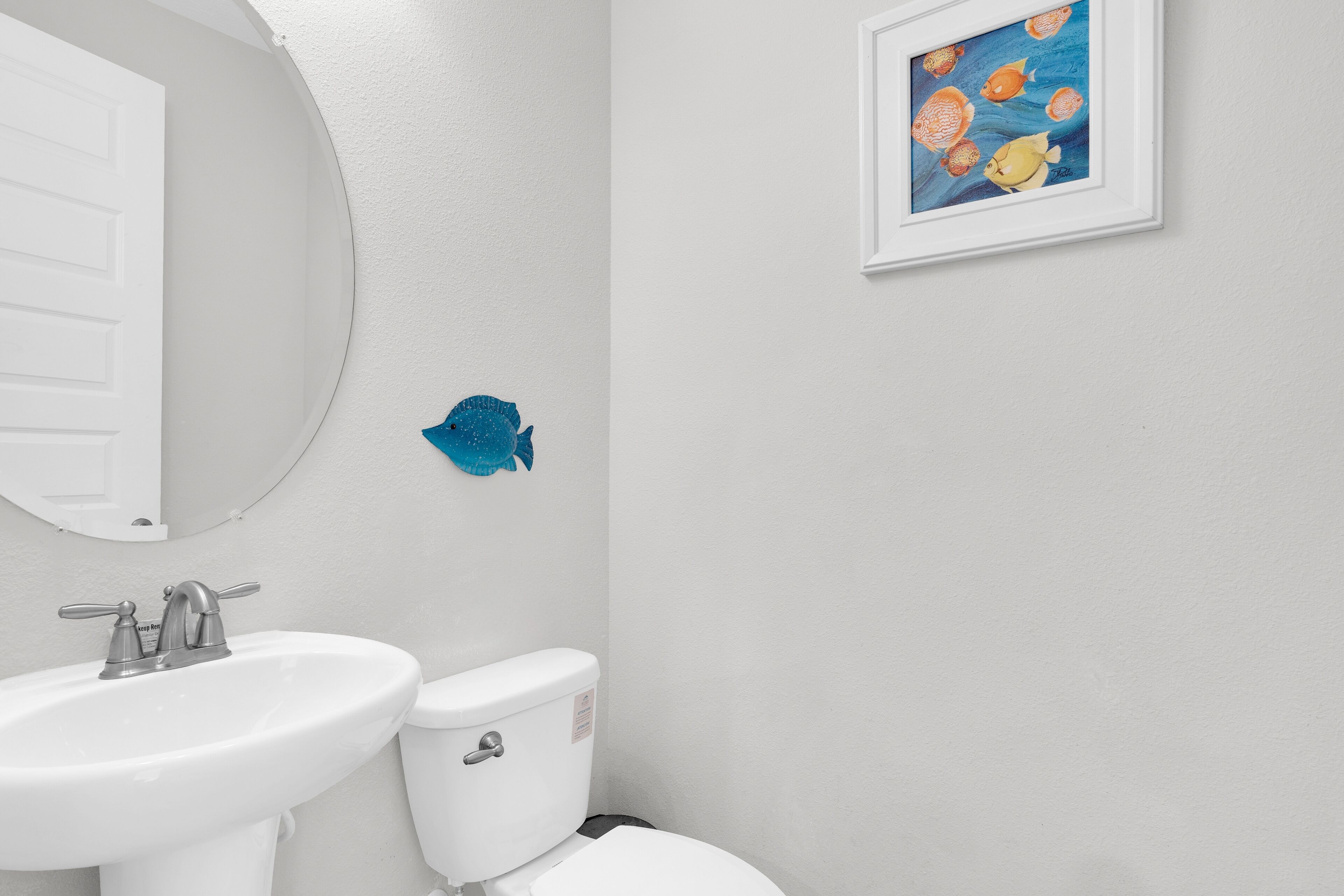 Een badkamer met een wit wastafelmeubel, toilet en een lijst met een visafbeelding aan de muur.