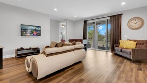 A modern living room with a large flat-screen TV, a sofa, a brown leather couch, and a wooden floor.
