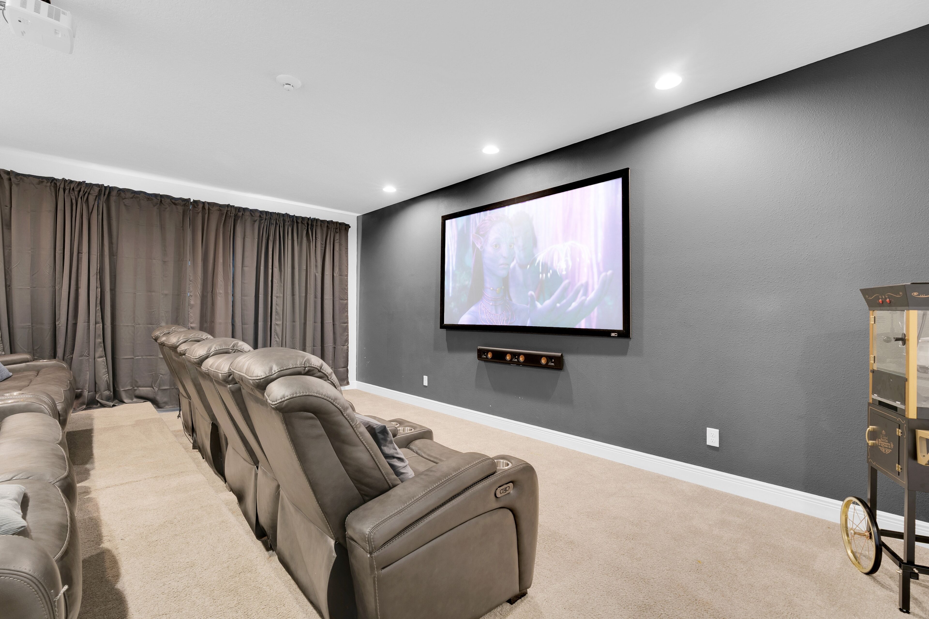 Sala de cinema com uma TV de tela plana grande fixada na parede, poltronas de couro reclináveis e piso coberto de carpete.