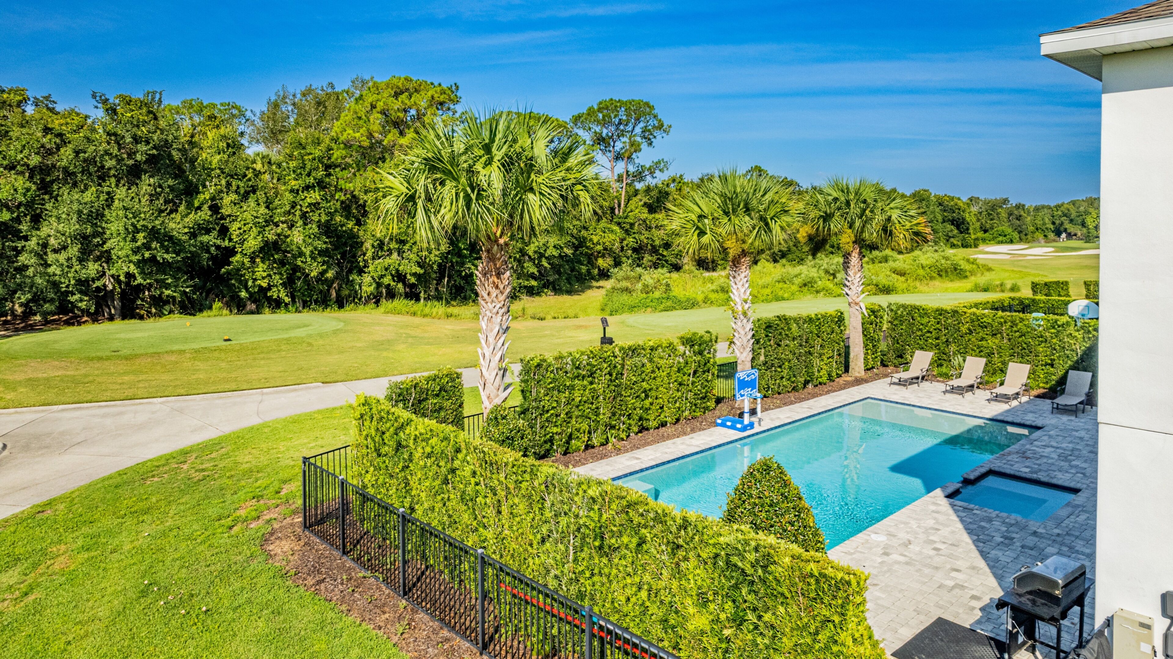 Una piscina rodeada de setos bien cuidados y palmeras, con un campo de golf al fondo.