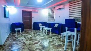 A room with a patterned floor, blue sofas, white tables, and a wooden door. - Hubbies Royale Hotel (Owerri)