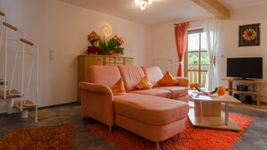 A living room with a sectional sofa, a television, a wooden cabinet, and a window with curtains. - Kleingesee approx. 5 km from Gössweinstein Holiday apartment Haus Sonnenscheim (Gößweinstein)