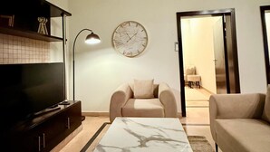 A living room with a TV, sofa, armchair, and a marble coffee table. - Designer & Spacious 2BHK Private Suite (Islamabad)