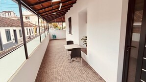 Un balcone coperto con pavimento piastrellato, un tavolo con sedie e una pianta in vaso.