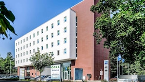 A multi-story hotel with a white facade and a red section, parking lot, and surrounding greenery. - Ibis Budget Augsburg City (Augsburg)