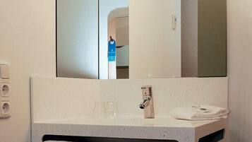 A bathroom with a large mirror, a sink with a faucet, two towels, and a light fixture.
