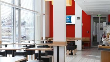 Un restaurant moderne avec des tables et des chaises, de grandes fenêtres et un mur d’accent de couleur rouge.