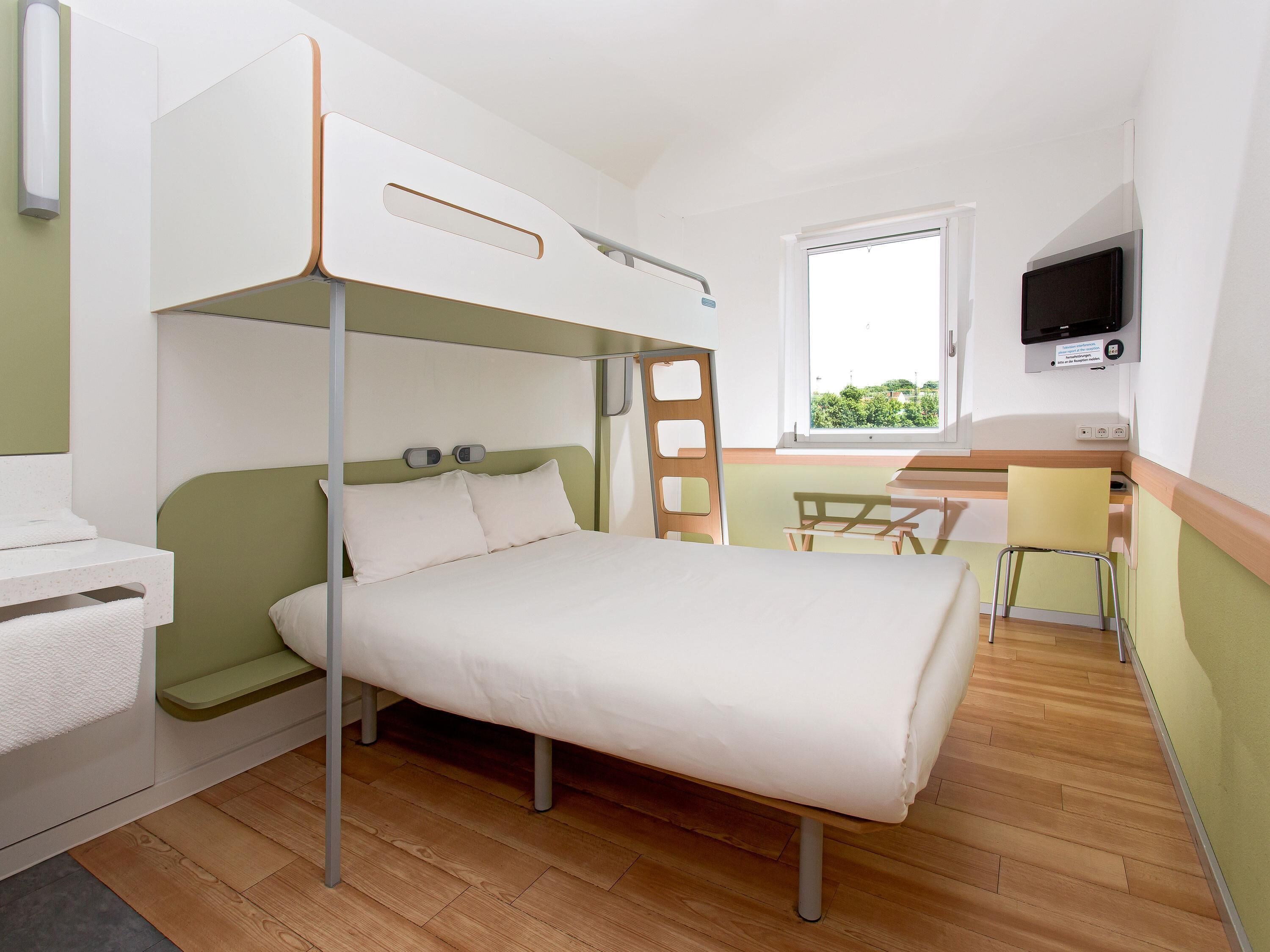A bunk bed with a desk and chair, a television, and a window with a view of greenery.