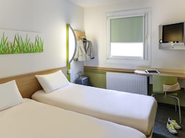 Una habitación de hotel con dos camas, un escritorio con una computadora, una ventana y un radiador.