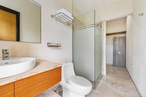 A modern bathroom with a large sink, toilet, and glass shower enclosure. - Ocean View 3BR Condo, Pool, Walk to Beach at Pájaro de Fuego | Casa Vista Ballena (Sayulilla)