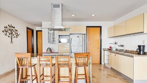 A modern kitchen with a central island, wooden chairs, and a stainless steel range hood.
