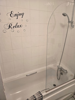 A bathroom with a glass-enclosed shower, a white tiled wall, and a towel rack. - Seaview 2 Double bed Apartment 2nd Floor (Llandudno)