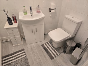 Une salle de bain avec un lavabo, des toilettes et un meuble de rangement blancs, un tapis à rayures et une poubelle.