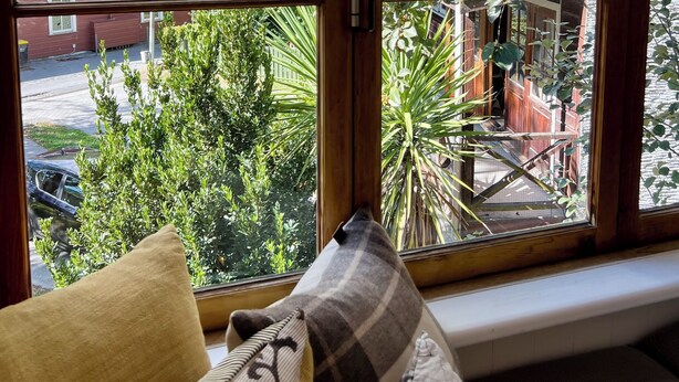 A room with a large window offering a view of a residential area, a bench, and a sofa with cushions. - Cosy cottage in the centre of historic Arrowtown (Arrowtown)