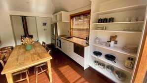 A compact kitchen with a wooden dining table, white cabinetry, and a built-in shelf with kitchenware. - Cosy cottage in the centre of historic Arrowtown (Arrowtown)