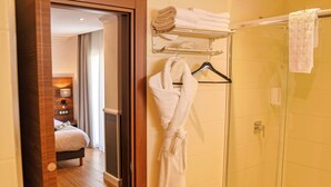 Un baño de hotel con ducha de vidrio, un perchero con toallas dobladas y una bata colgada en la pared.