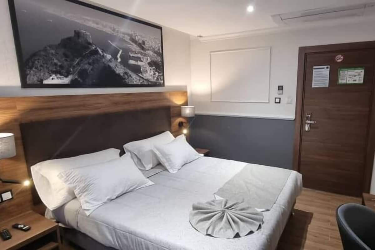A hotel room with a bed, bedside table, lamp, and a framed picture on the wall.