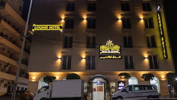 A hotel with a prominent sign reading "Lounis Hotel" and "Oran by Atlantis" in Arabic. It features a symmetrical facade with evenly spaced windows and a central entrance.
