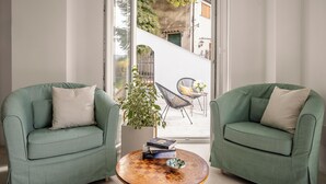 A room with two green armchairs, a round wooden coffee table with books and a bowl, and a view of a street and greenery outside. - ElChiMa by Wonderful Italy (Polizzi Generosa)