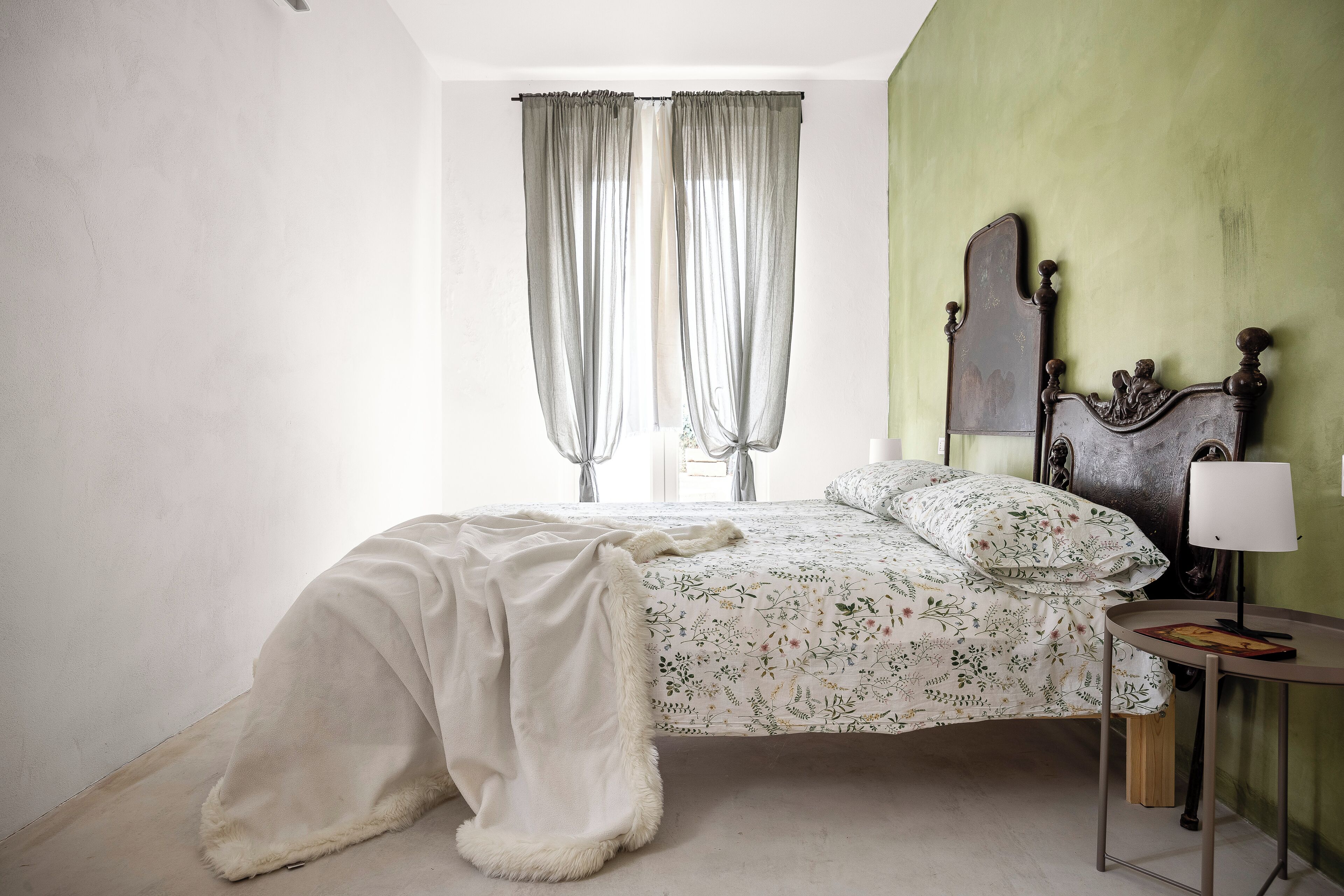 Un dormitorio con una cama, una mesita de noche con una lámpara y una ventana con cortinas.