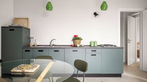 A modern kitchen with a glass dining table, green chairs, and a blue island. - ElChiMa by Wonderful Italy (Polizzi Generosa)