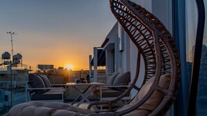 Un lounge en la azotea con sillas de mimbre y una mesa, con vistas a un atardecer.