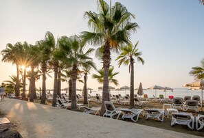 A beachside lounge area with rows of white sun loungers and palm trees. - TelMar Sea View Apartment 5min walk Beach (Oroklini)