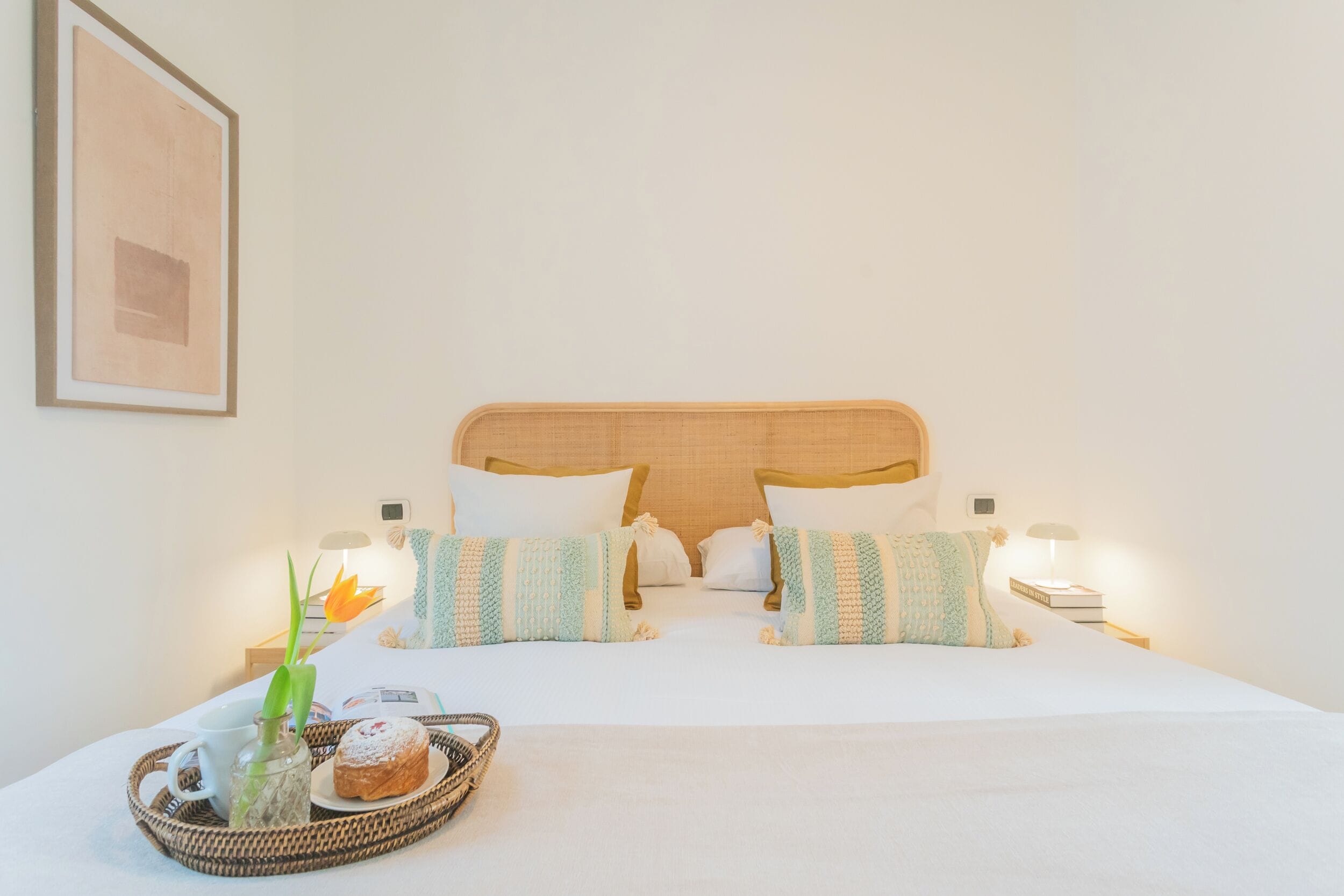 Een net opgemaakt bed met witte lakens, twee kussens met strepen en een nachtkastje met een lamp.
