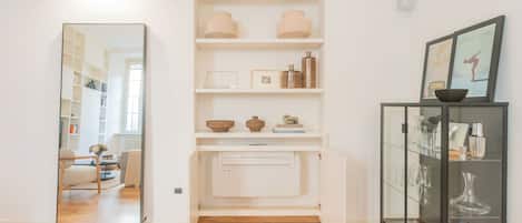 A modern interior with a wooden floor, a white shelving unit with decorative items, and a glass cabinet with glassware.