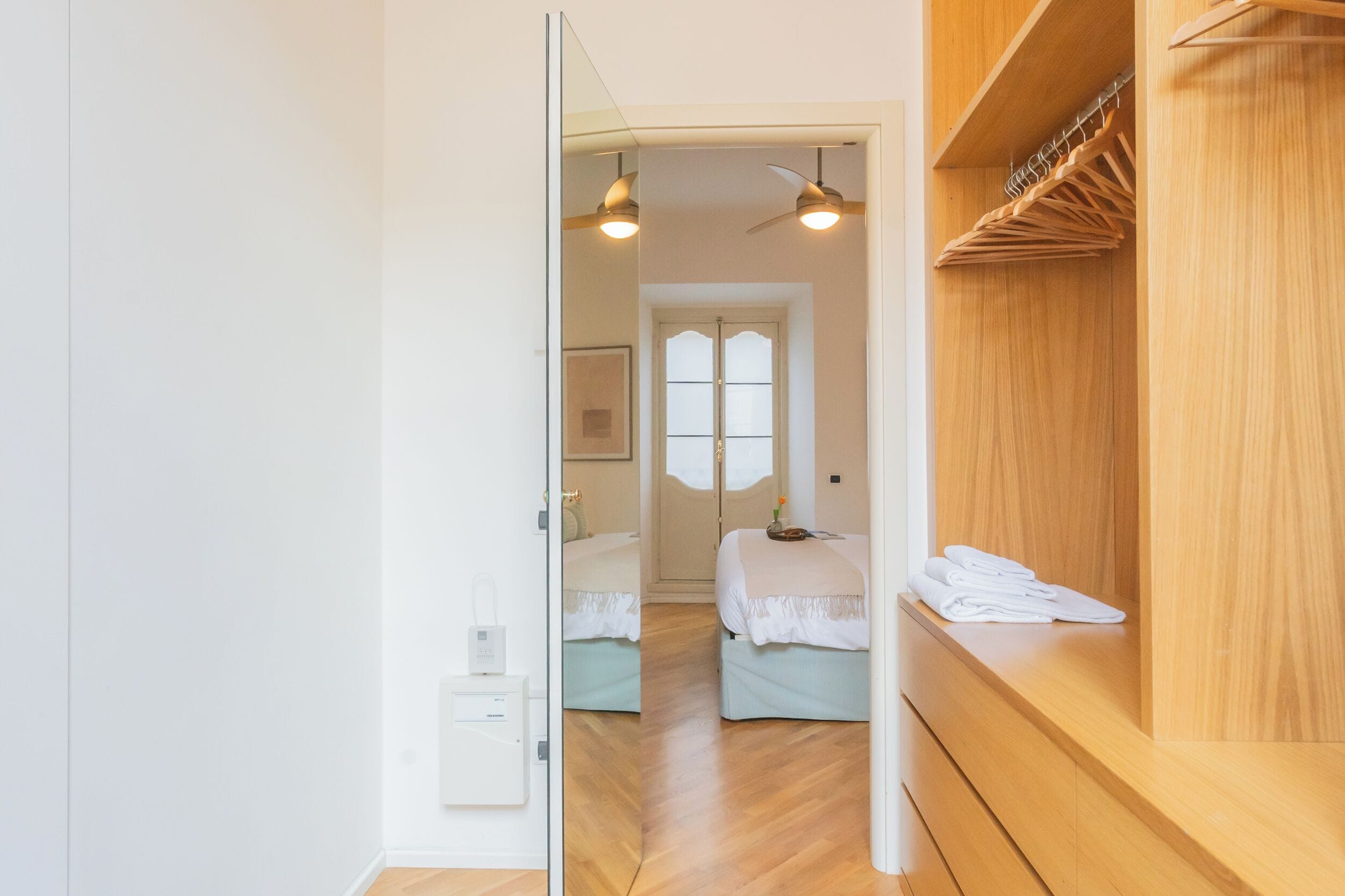 A modern bedroom with two beds, wooden wardrobe, and ceiling fans.