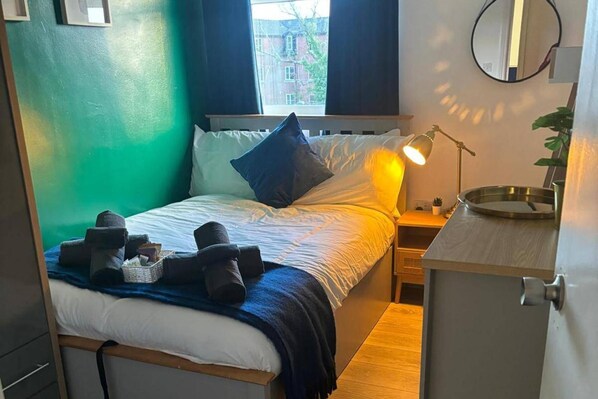 Habitación de hotel pequeña con cama, mesita de noche, lámpara y un espejo.