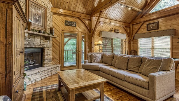 A cozy log cabin interior with a stone fireplace, wooden furniture, and a large window. - CABIN FEVER - Total Seclusion in Wears Valley! (Sevierville)