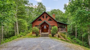 A log cabin with a porch and a gravel driveway, surrounded by dense forest. - CABIN FEVER - Total Seclusion in Wears Valley! (Sevierville)